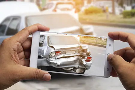 A hit-and-run victim taking a picture of the damaged rear end of their car on their phone.