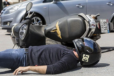 An injured rider lies next to his scooter in the road after a crash