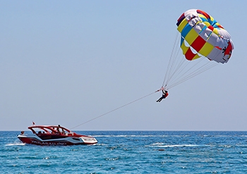 A person parasailing over the water, towed by a boat through clear blue sky.