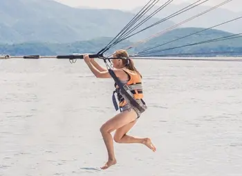 A woman in a parasailing harness gets her feet wet as she descends to fly just above the water.