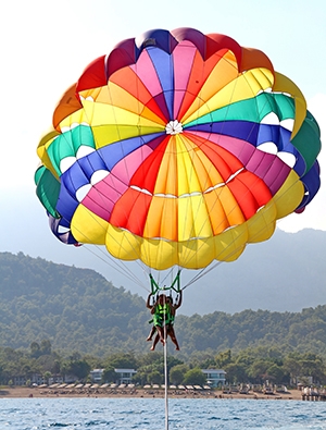 A large multi-colored parasailing canopy ascends into the air as it is towed across the water.