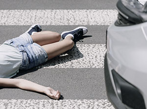 An injured pedestrian laid on the street on a crossing, next to a car.
