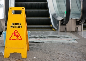 An escalator with a slip and fall hazard spillage and a warning sign next to it.