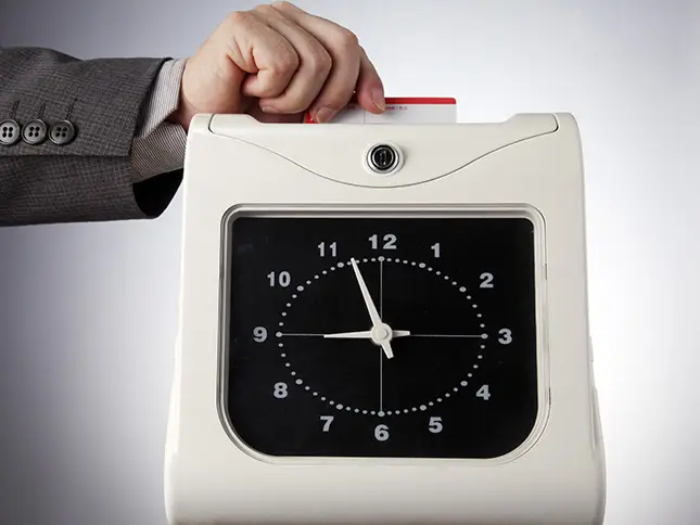 underpaid wages: a worker punching their time card in a company clock