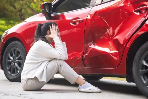 Young woman standing beside damaged car after traffic collision on roadside